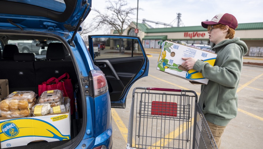 blue car in hyvee parking lot with person loading box into the back