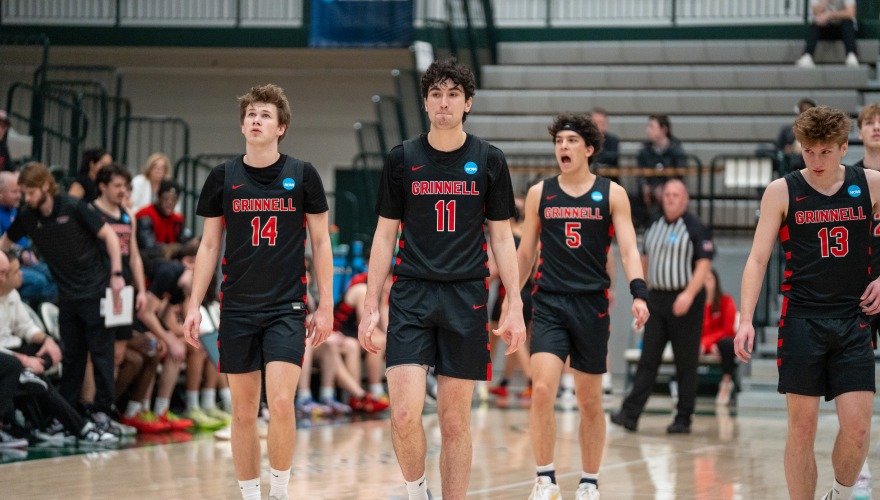 Four Grinnell men's basketball players wearing black uniforms walking on the court