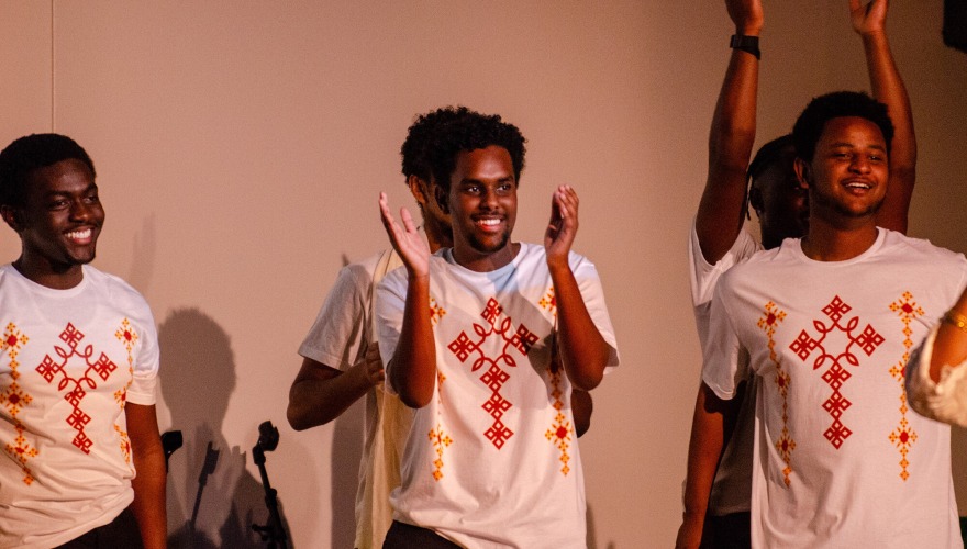 men clapping on stage in white shirts with orange lettering 