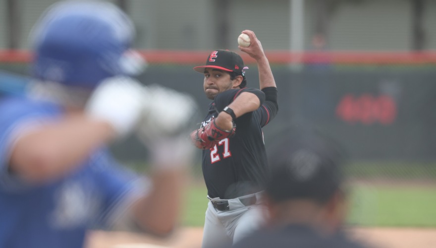 Pitcher in the middle of their windup with opposing team batter in the foreground.