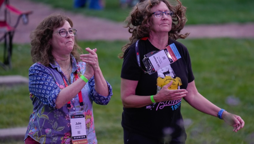 Two alums clap and dance along with the performance on stage.