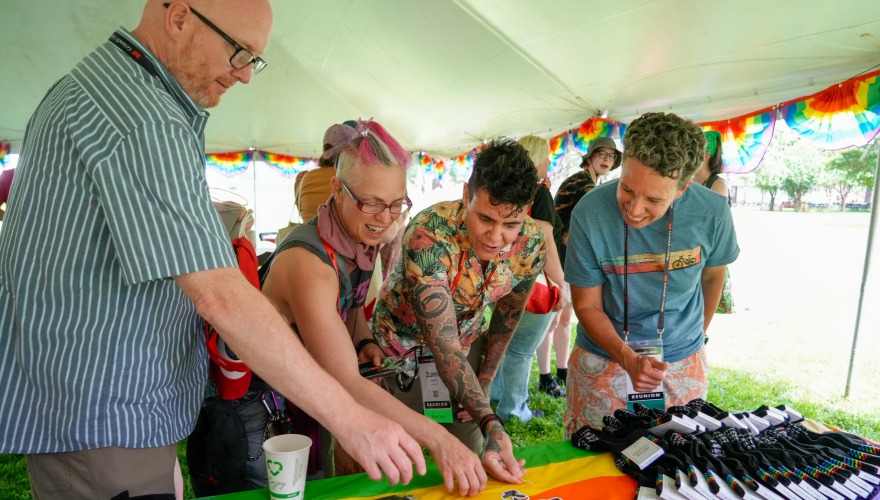 A group of alumni attending the Rainbow Alumni event look at stickers on the merch table.