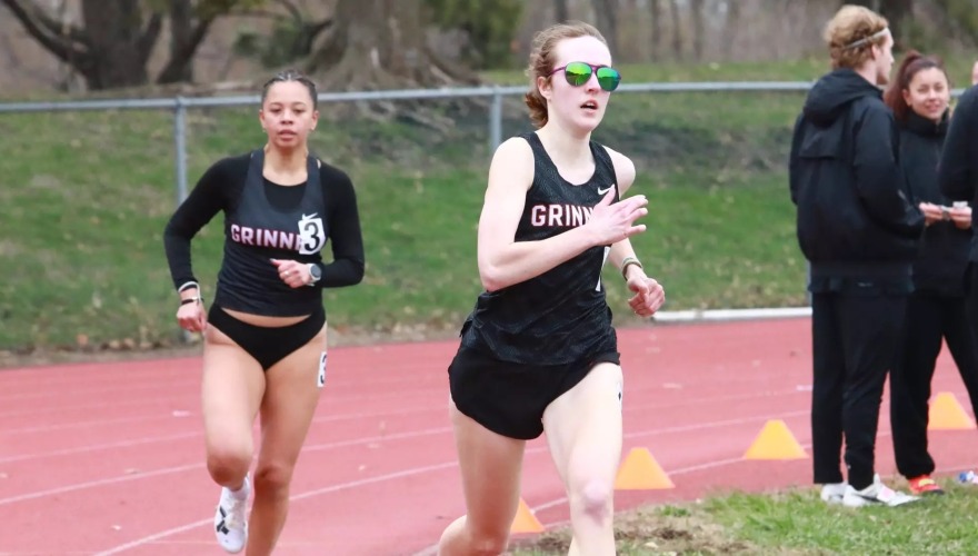 A student-athlete running on an outdoor track with an opponent close behind.