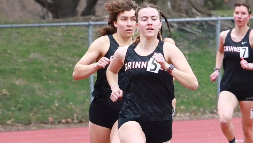 A student-athlete running on an outdoor track with opponents following close behind.