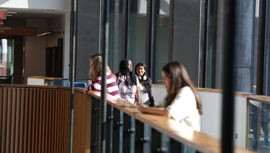 Students stand at a banister and walk across a walkway in the Humanities and Social Sciences Center.