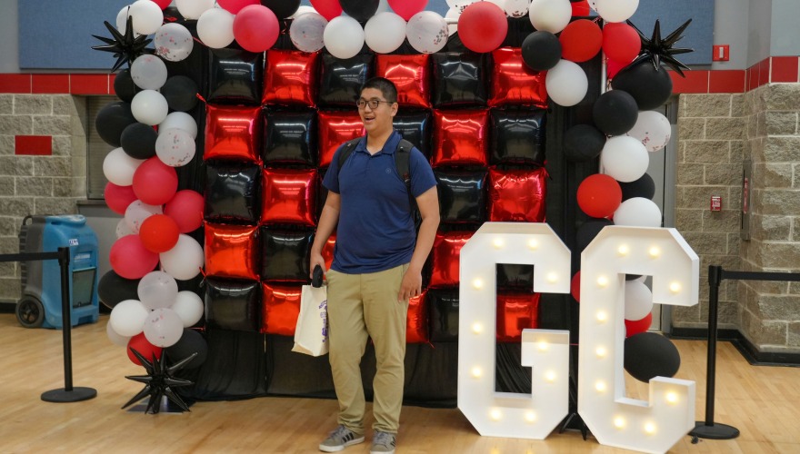 Student poses for a photo in front of a balloon display in the Harris Center at move-in check-in.