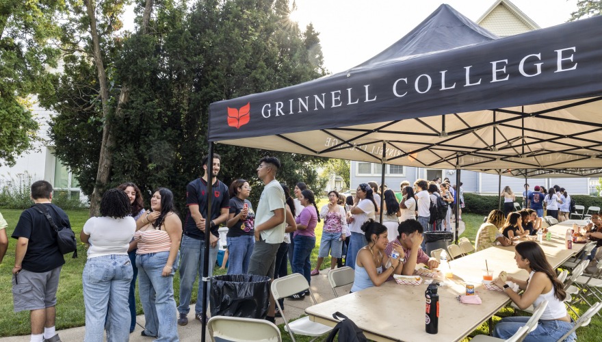 Students sit at picnic table while others wait in line for food outside