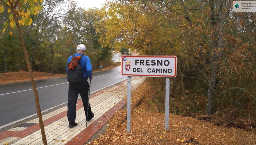 Professor Will Freeman walking on a sidewalk in Spain passing a road sign that says Camino