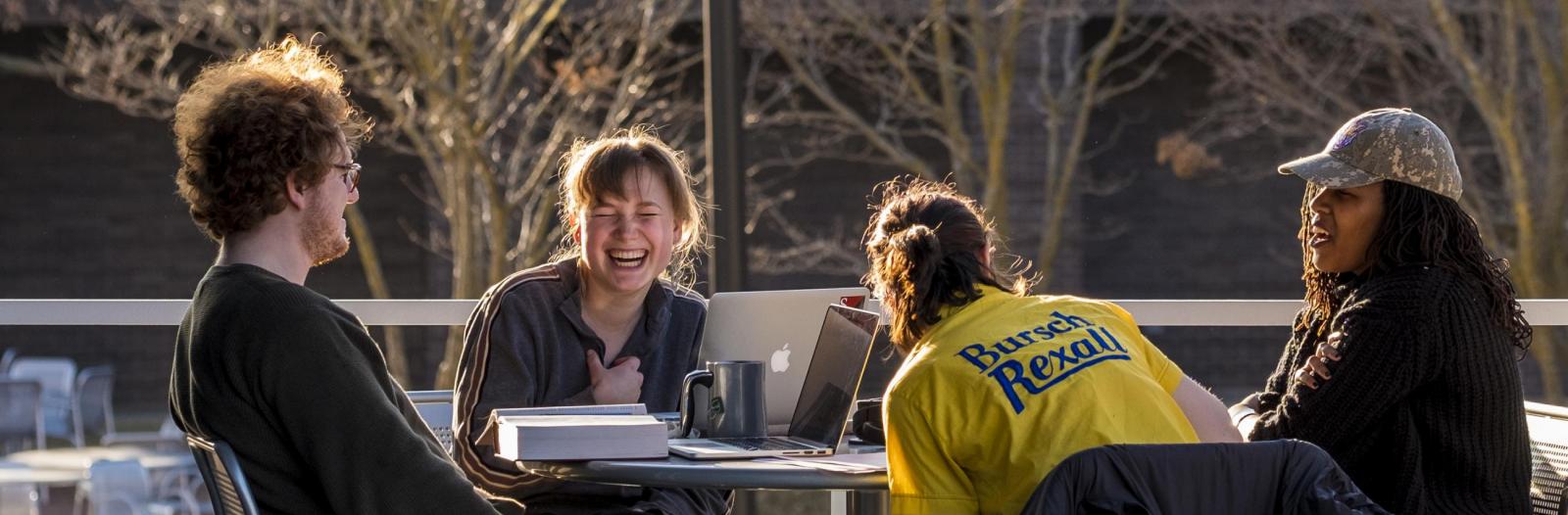 4 students laugh at an outdoor table