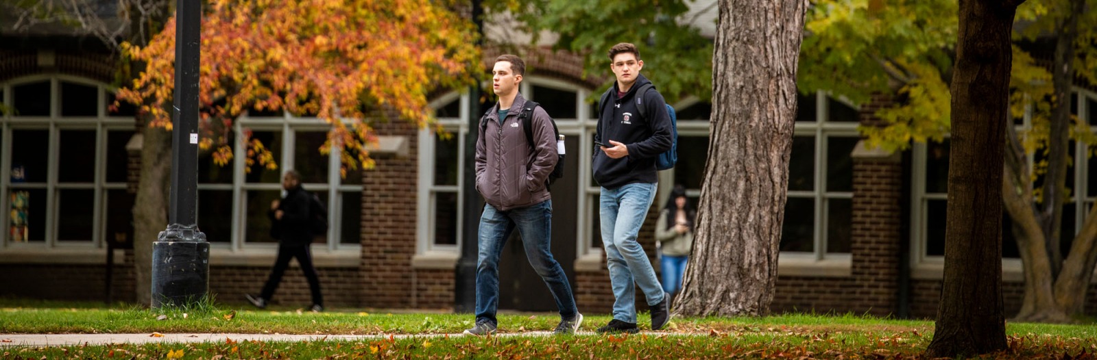 Students walk on campus with colorful fall leaves