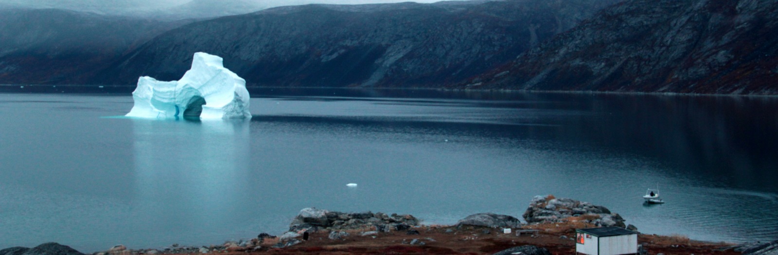 Lone iceberg in a sea of water near shore with a shack in the foreground