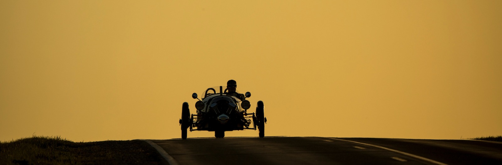 A Morgan 3-wheeler heading down the highway at dusk