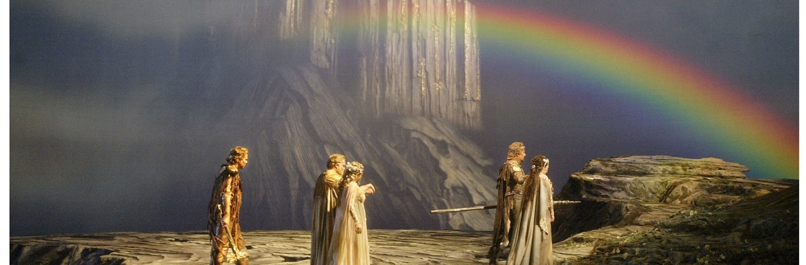 A scene from Wagner's Das Rheingold. People walking toward a rainbow with a mountain or castle in the background.