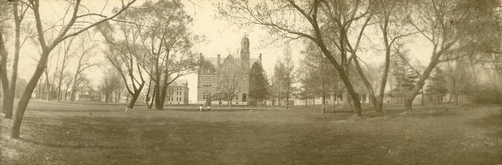 Sepia toned image of campus with only a few building and two women sitting on the lawn 