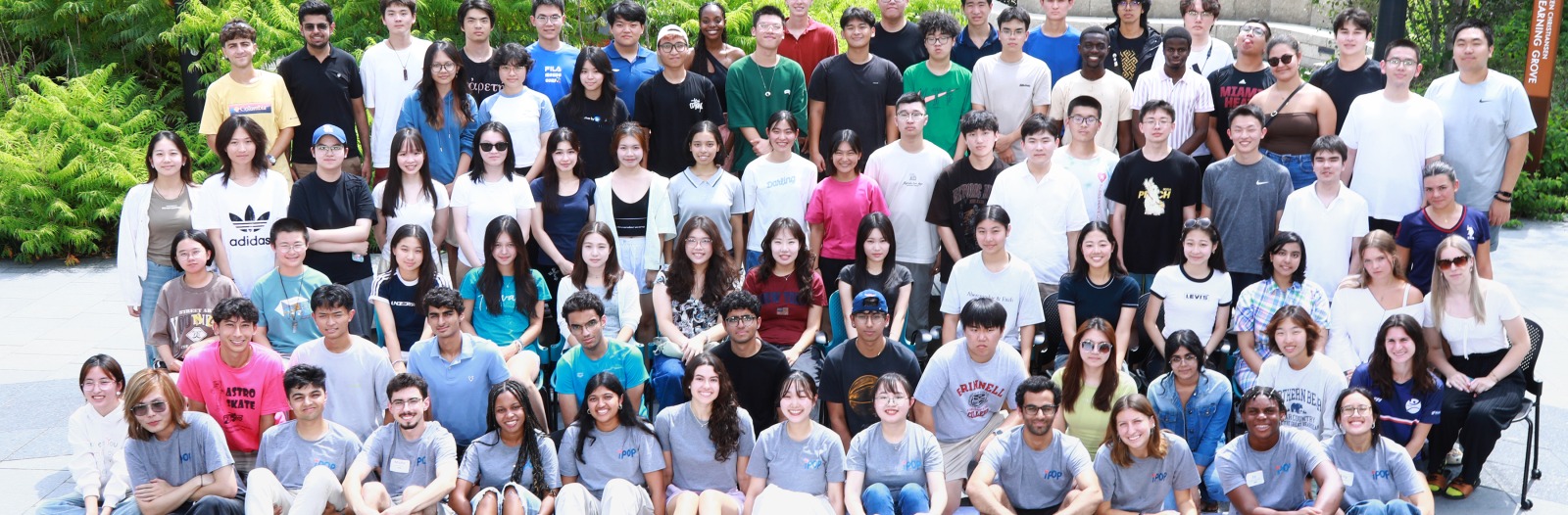 A large group of people standing outside in a grey courtyard, smiling at the viewer
