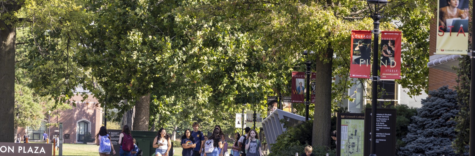 student walking to class outside with trees and campus banner