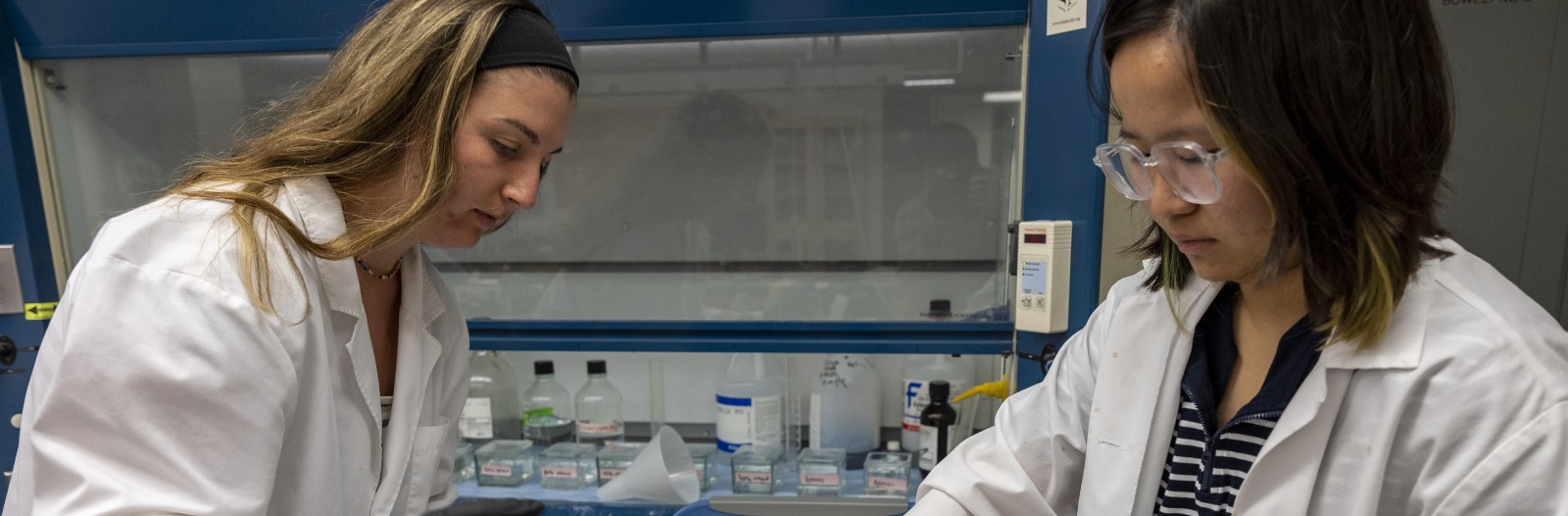 Two students in lab coats work on their research.