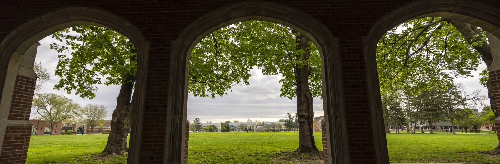 A view of the Grinnell College campus through three arches of a loggia across Mac field.