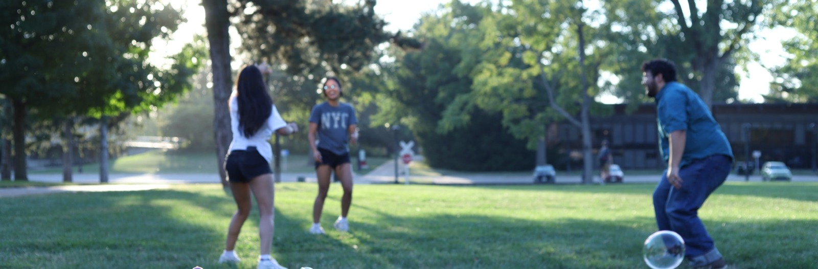 Three students play vollyball in the grass outside south campus
