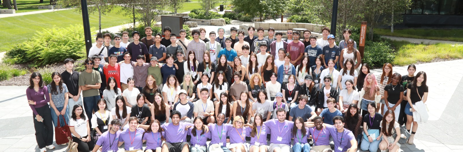 A large group of people standing outside in a grey courtyard, smiling at the viewer