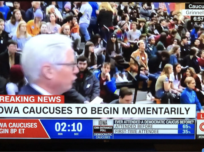 CNN newscast from the Iowa Caucus with a crowd of people seated in bleachers in the background