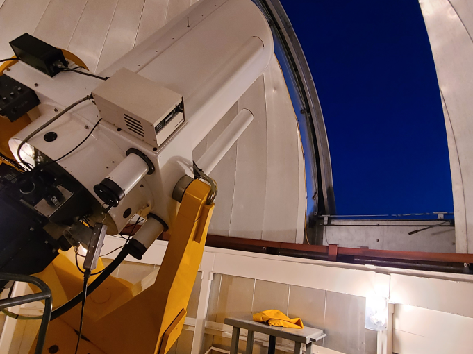 A rectangular white telescope points towards an opening in the domed building with a dark night sky