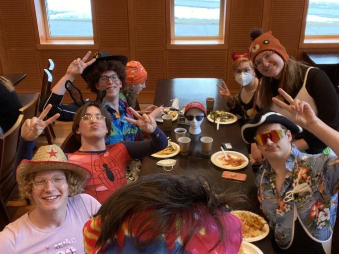 Swim and dive team members dressed up in funny costumes ranging from pirates to cowboys to spiderman to reindeer all pose in front of the selfie in a dining hall room. I have shades and a bandana on as I take the photo.