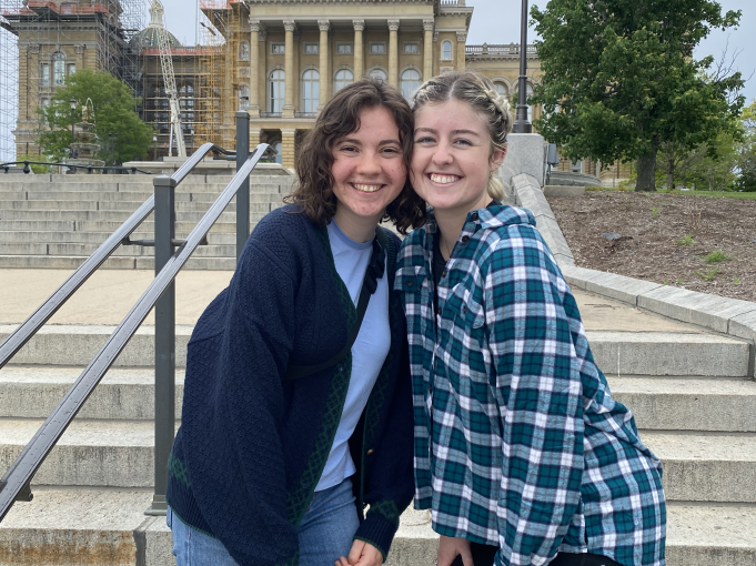 Me and my later roommate do sorority squats in front of the Des Moines capital steps. You can see a large yellow dome in the background.