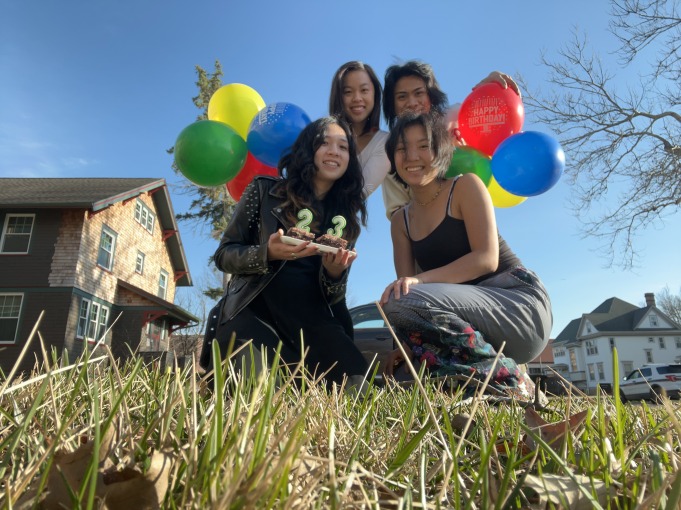 Mia and her friends crouch near the grass while holding colorful balloons.