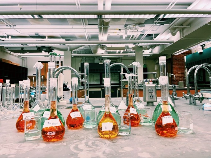 12 glass-made volumetric flasks and 5 glass-made measuring cups, all with different labels and hues or orange or green.