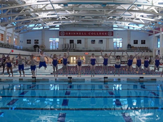 The synchronized swimming team take a group photo at the pool. They all jump into the pool at around the same time.