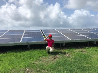 Person in red shirt and hat sitting in front of solar panels. 