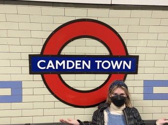 I'm sitting on a bench and shrugging next to the "Camden Town" sign on the subway.