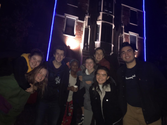 Me and my six friends smile in front of the Gates Tower with blue fluorescent lights. I'm on one of my friend's back.