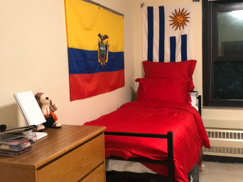 My side of the dorm room. There's a big Ecuadorian flag on the wall right next to my bed. My bed has vibrant red blankets and pillows.