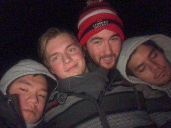 Me and my three friends all huddle up together in the freezing dark cold. We are all wearing winter hats.