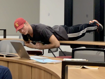 I'm doing a plank on the desks in a classroom in the Humanities and Social Science Center (HSSC). I'm goofing around and having fun with my friends