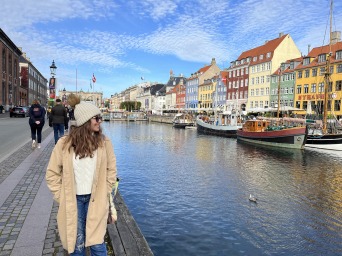 Andrea strolls along a canal in Denmark with a row of colorful housees and small boats