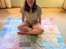 Ailsa sitting crosslegged on a multicolor pastal quilt