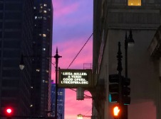 Sunset with viewed between two buildings, one with a hanging lit sign 
