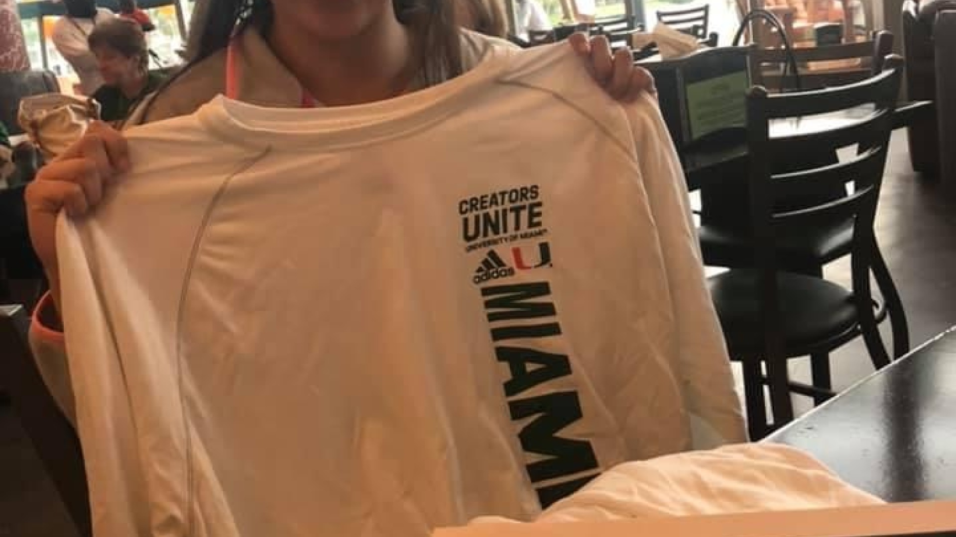 Girl holding up Miami Basketball shirt. 