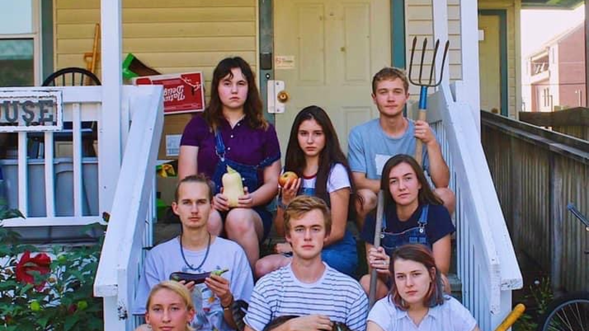 students sitting on porch steps holding farm instruments and produce