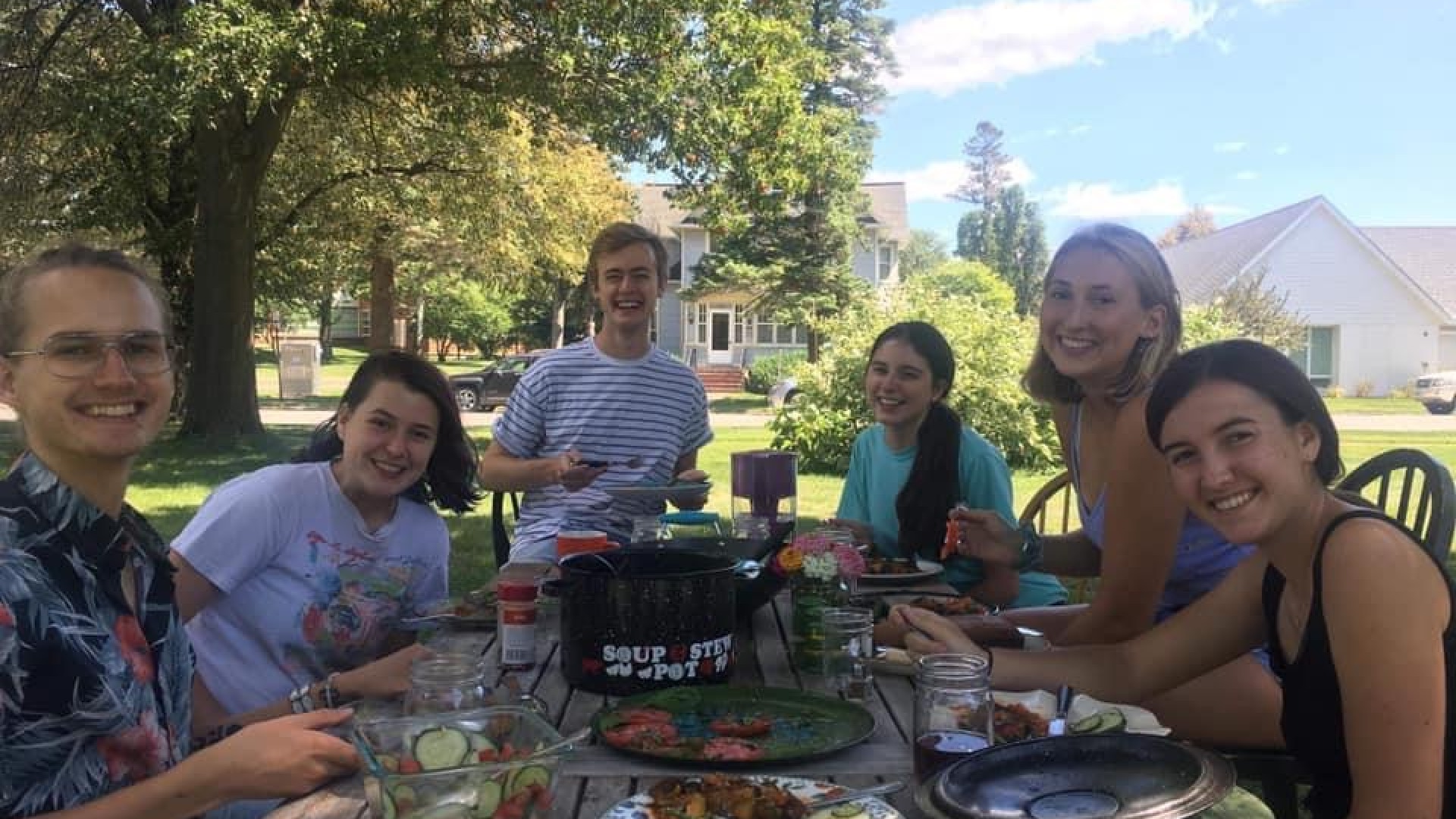 Students around a picnic table eating, large pot that says soup and stew pot in center of table