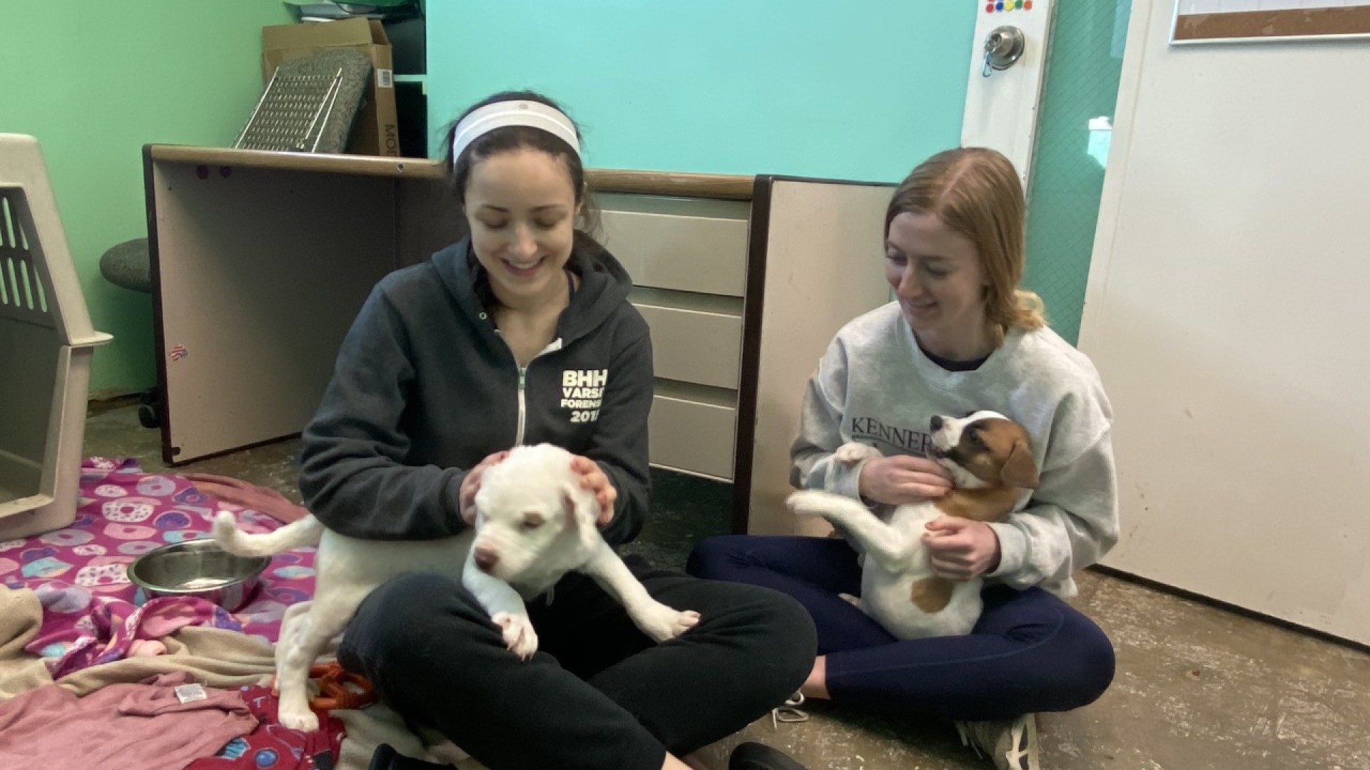 one woman pets a white puppy and the other a brown and white puppy