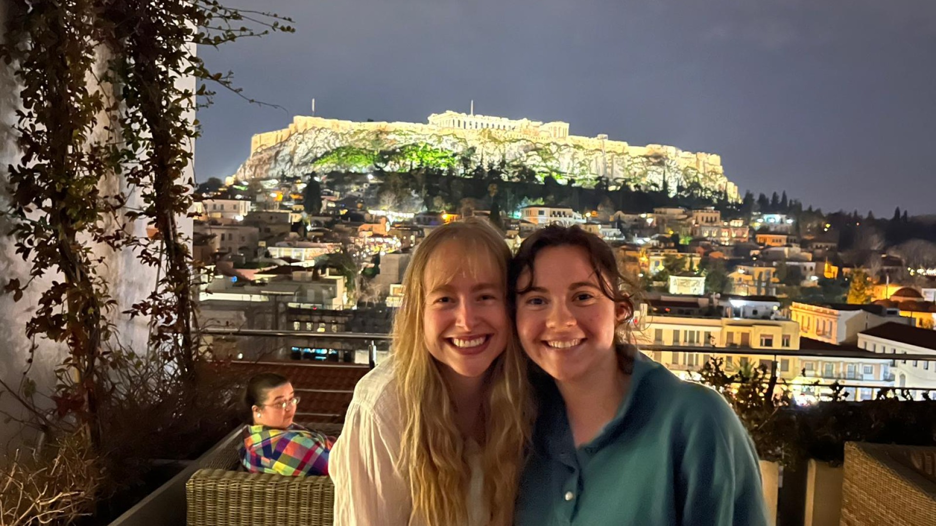 Elisabeth, my fellow Senior Interviewer, and I are on a hotel rooftop and we smile together with beautifully lit Athens in the background