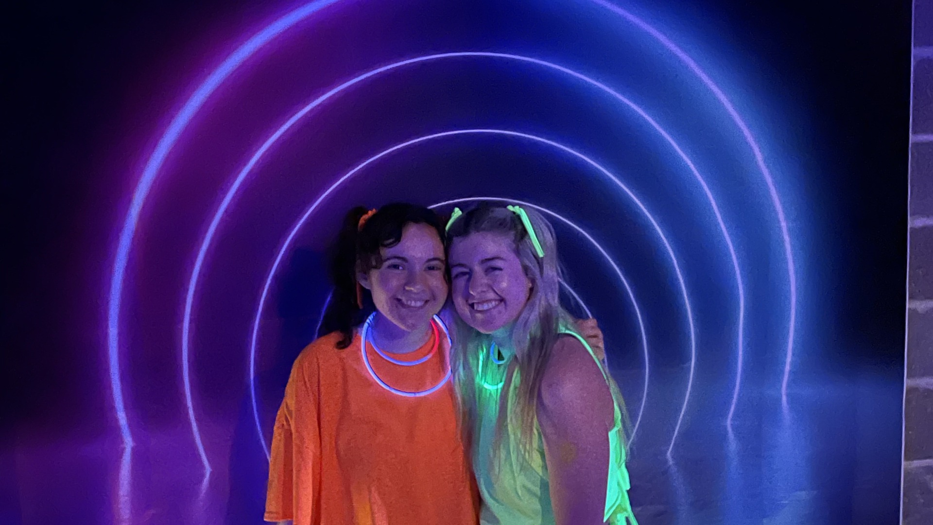 My roommate and I are dressed in neon shirts and hairties with fluorescent rings around our necks and wrists. We pose together in front of the neon half-dome shaped wall in Disco Harris!