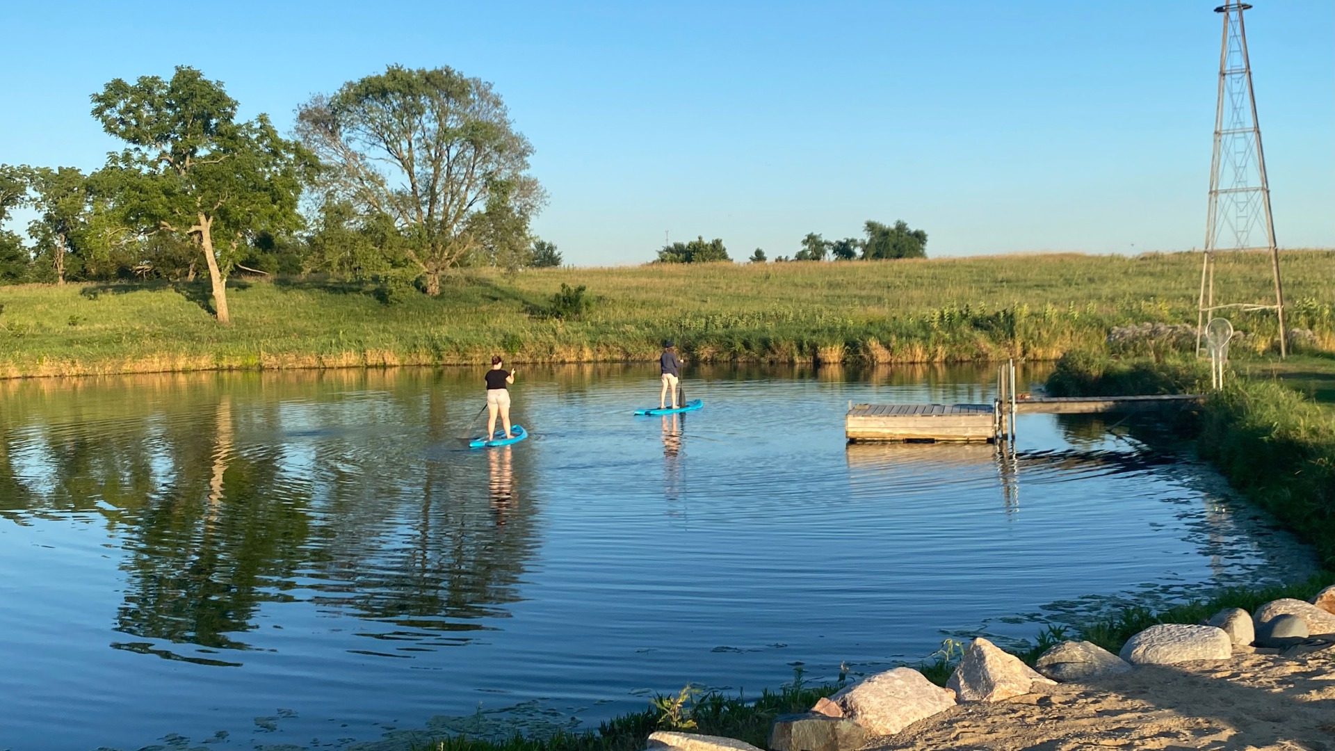 Pond for paddle boarding in Kellogg, Iowa. The waters are clear blue, trees are vibrant and healthy, and skies are very blue.