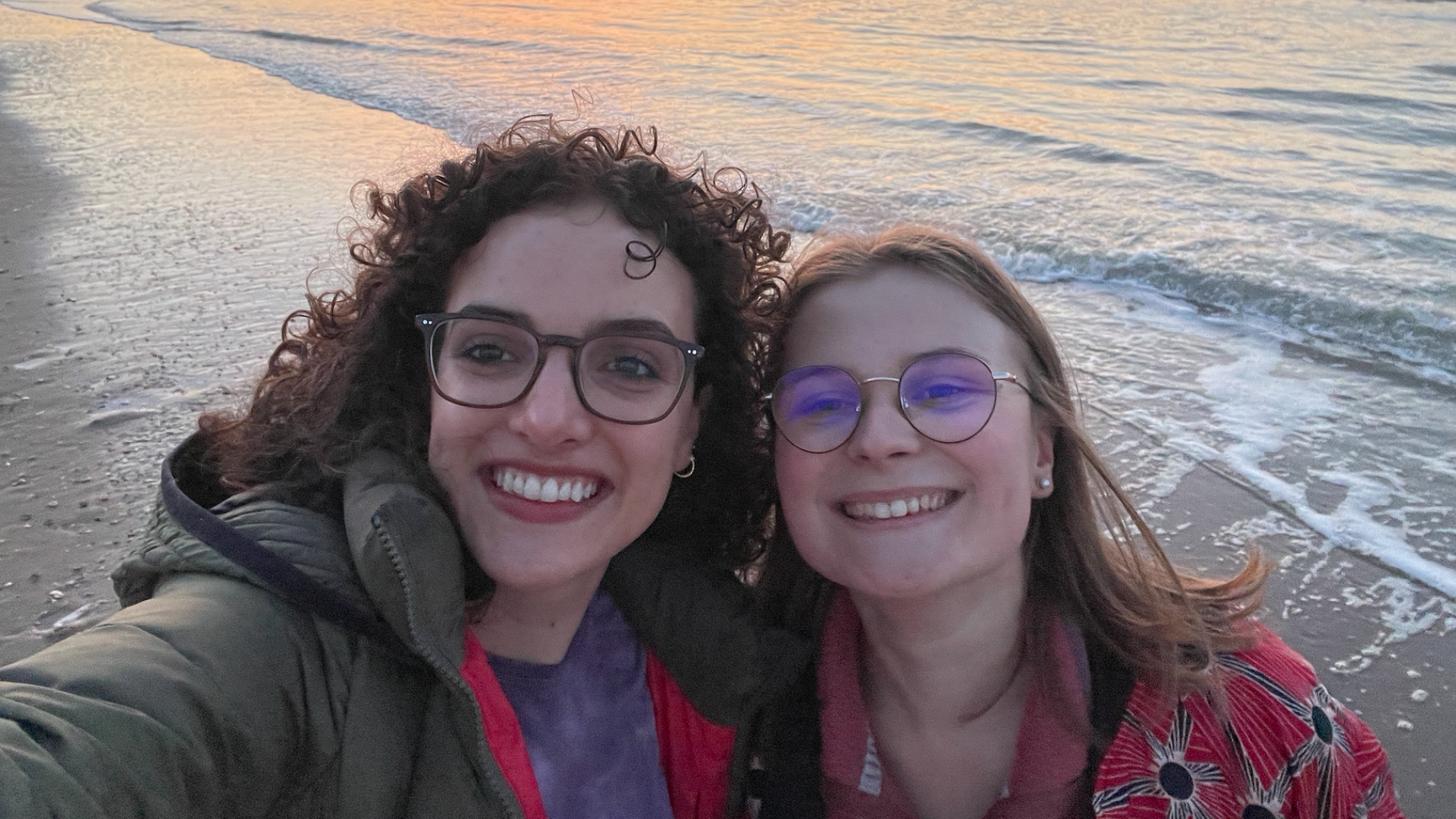Me and my friend smile in front of the beach! It's sunset and the orange rays light up the ocean beautifully.