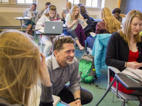 Tyler Roberts squatting next to students while teaching a course