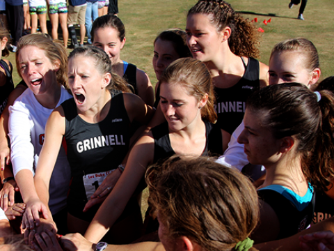 Grinnell's womens track team stack hands in a huddle and shout